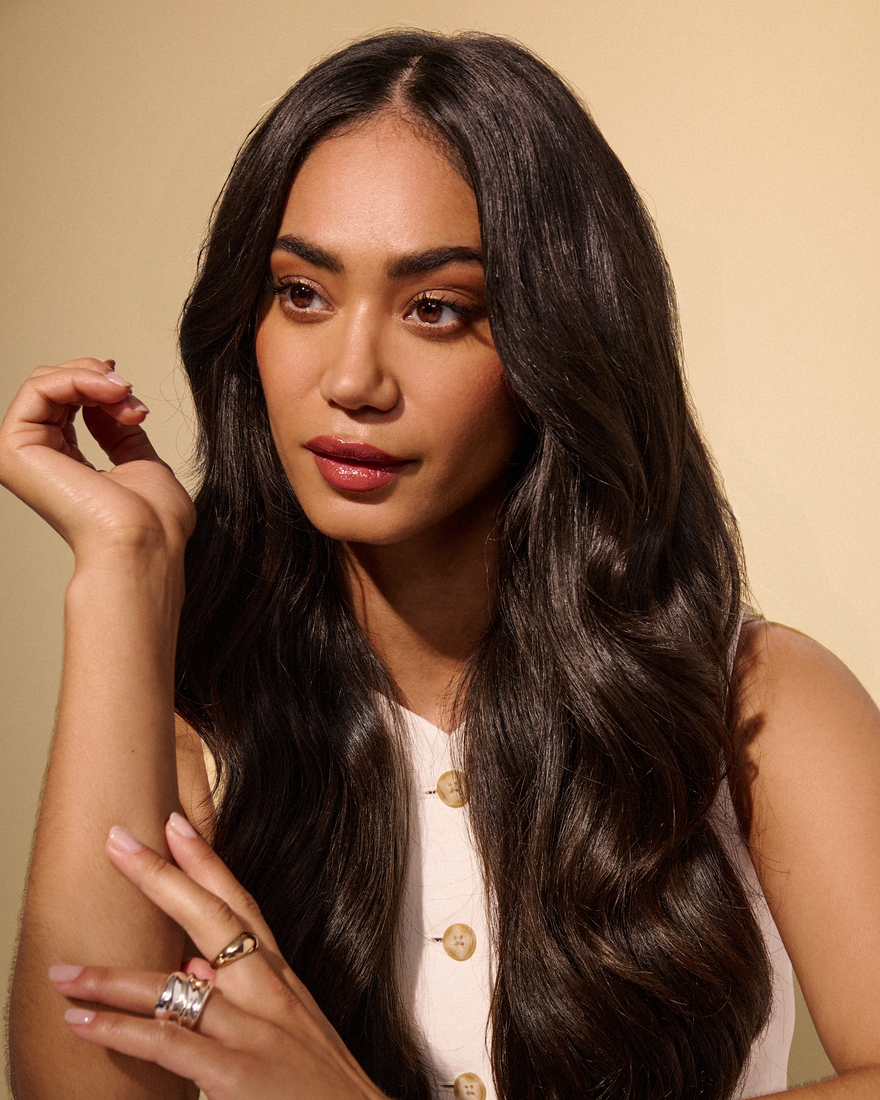 A woman with long black hair enhanced by extensions, wearing a ring on her finger, exudes elegance and style. 