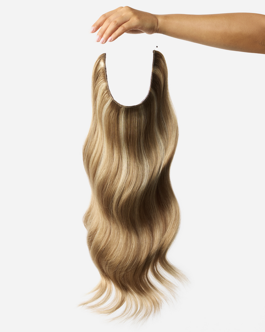 A woman's hand gracefully holds a long dark ash blonde blend wig, showcasing its vibrant color and texture.