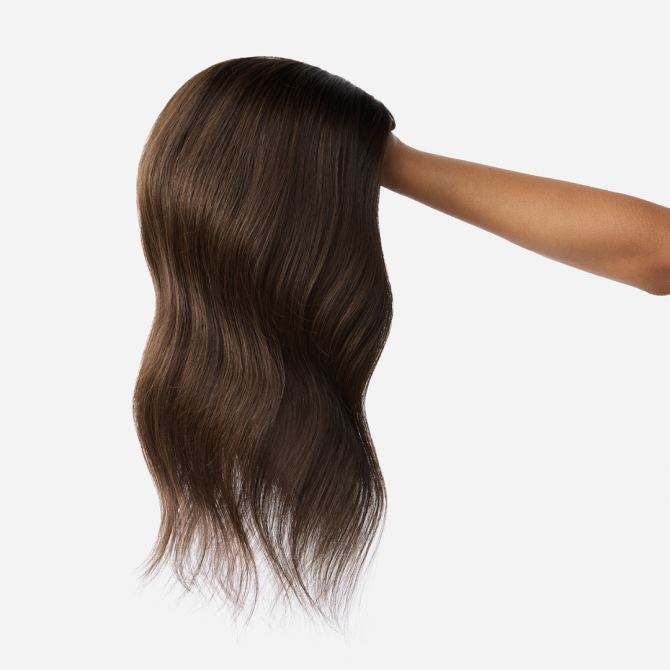 A woman's hand gracefully holds a long brown wig, showcasing hair extensions for styling and versatility.