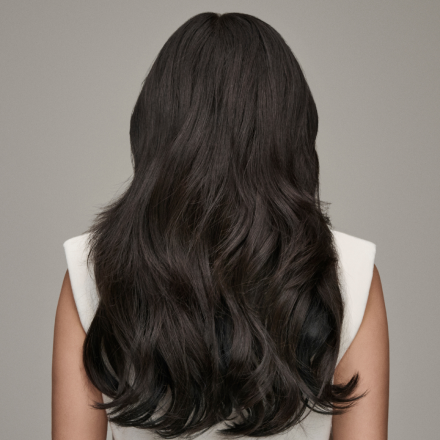 A woman with long, dark hair, enhanced by hair extensions, is seen from the back, showcasing her flowing locks.