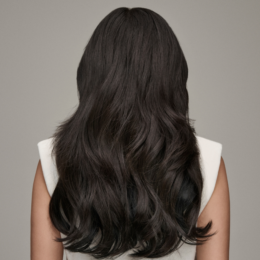 A woman with long, dark hair, enhanced by hair extensions, is seen from the back, showcasing her flowing locks.